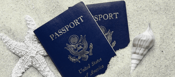 US passports in white sand between a starfish and a seashell